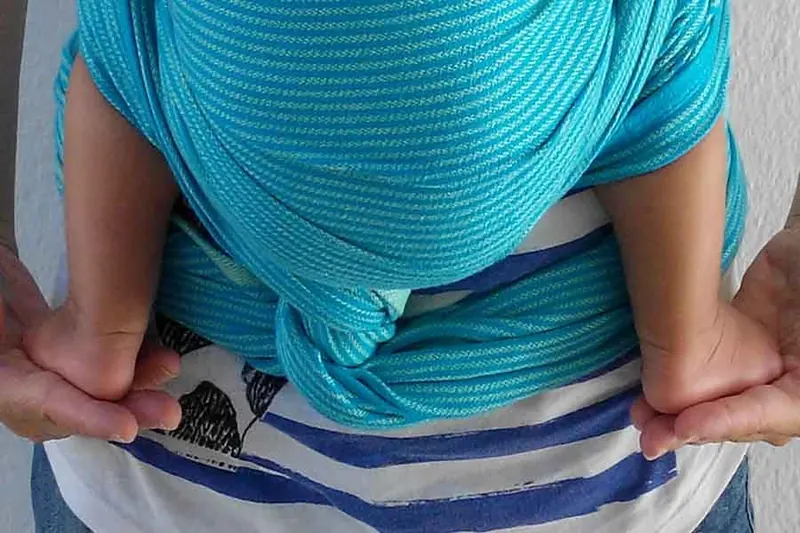 Una madre lleva a su bebé a la espalda con un fular, en una sesión de porteo
